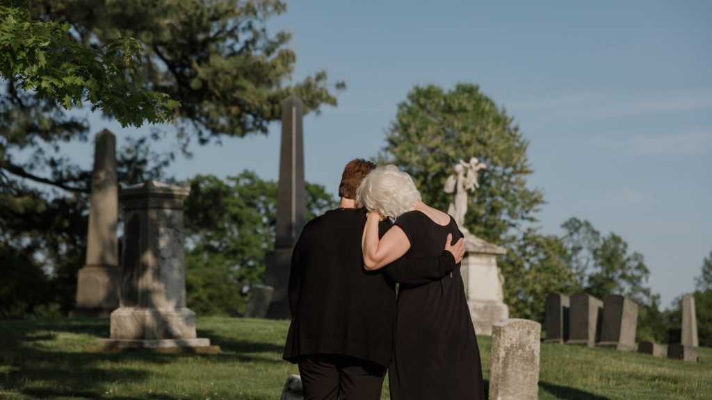 A woman comforting another woman at a cemetery.